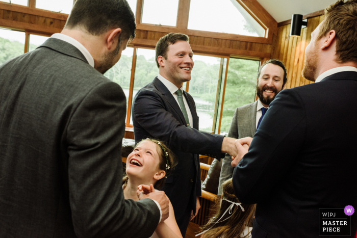 A top Hebron, Connecticut wedding photographer captured this picture at Easterseals of Oak Hill Camp Hemlocks as the groom and a flower girl smile and embrace others in celebration just following the wedding ceremony