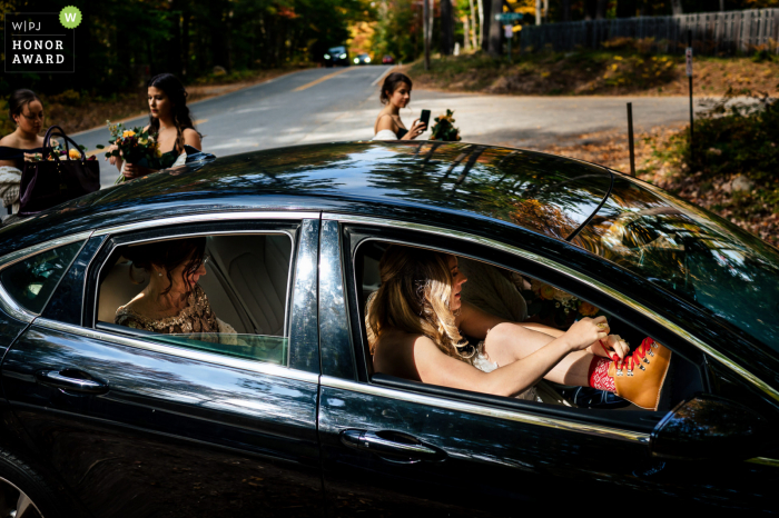 Uma imagem de casamento excepcional de Jackson NH por um fotógrafo profissional de New Hampshire exibindo a noiva amarrando as botas no carro enquanto se preparava para ver o noivo