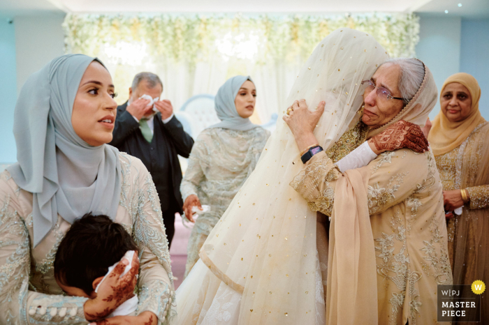 Der Hochzeitsdokumentarfotograf aus Birmingham, Großbritannien, erstellte dieses Bild einer muslimischen Braut, die sich von ihrer Familie verabschiedet, während ihr Vater im Hintergrund weint Der Hochzeitsdokumentarfotograf aus Birmingham, Großbritannien, erstellte dieses Bild einer muslimischen Braut, die sich von ihrer Familie verabschiedet, während ihr Vater im Hintergrund weint