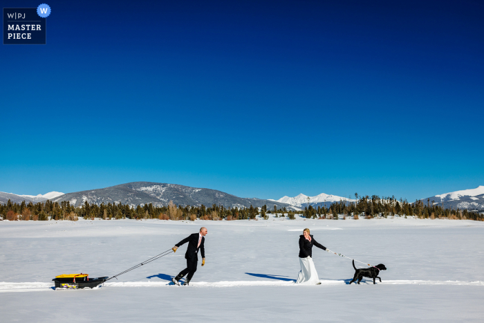 Colorado wedding image of the bride and groom hiking to ceremony on the winter snow with two dogs during an ice fishing elopement