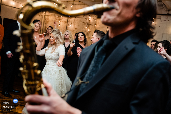 Documentary photography from The Art Factory wedding venue in Paterson NJ showing The bride was excited to have a saxophone player at the reception in a moment of celebration