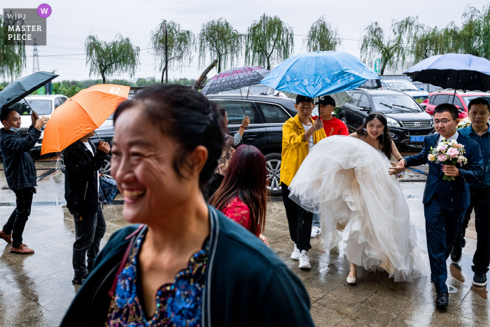 Documentairefotografie van een bruiloft in een hotel in Sichuan terwijl vrienden de bruid in de regen begroeten, terwijl de moeder van de bruid vrolijk lacht, maar de paraplu lijkt de bruid niet te bedekken