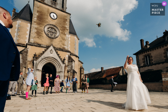 Documentary photography from a wedding venue in Mézières-en-Brenne, Indre of The throwing of the brides bouquet in front of the Church