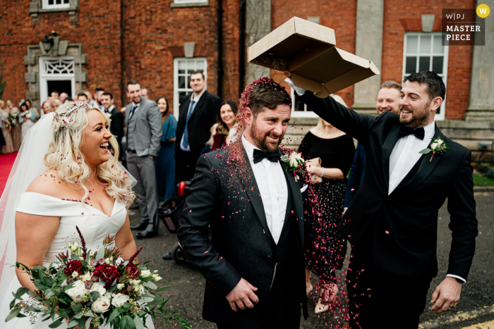 Melhor fotografia de casamento do local Mottram Hall no Reino Unido capturando um padrinho jogando confete na cabeça do noivo Melhor fotografia de casamento do local Mottram Hall no Reino Unido capturando um padrinho jogando confete na cabeça do noivo