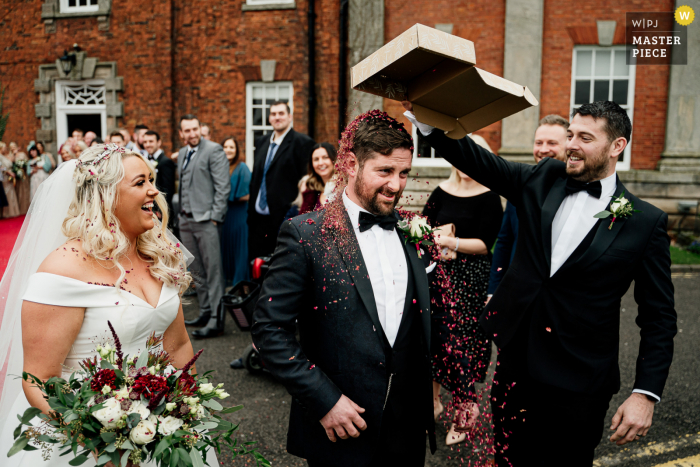 Best wedding photography from the Mottram Hall venue in the United Kingdom capturing a Groomsman tipping confetti over the head of groom