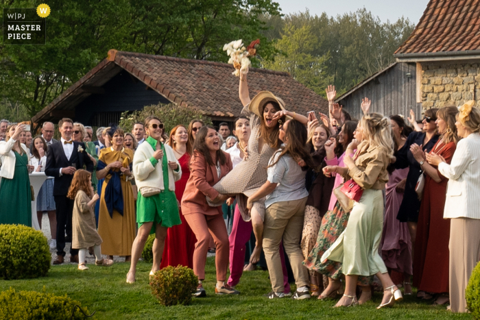 Lille based wedding and event photography shows a guest catching the tossed bridal bouquet during cocktail outdoors on the grass lawn