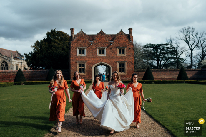 Dokumentalny fotograf ślubny w miejscu imprezy Doddington Hall w Lincolnshire w Wielkiej Brytanii, pokazujący pannę młodą przybywającą na ceremonię z druhnami