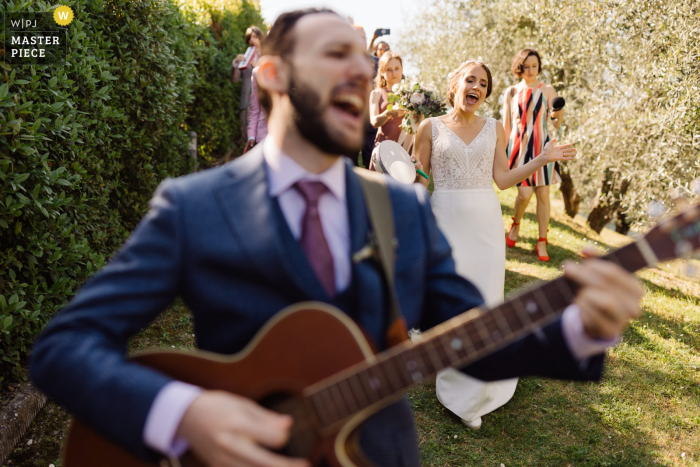 Beste huwelijksfotografie van een locatie in Guardastelle, San Gimignano, waarbij de bruidegom en de bruid zingen na de huwelijksceremonie terwijl ze wandelen met een gitaar en een groep vrienden