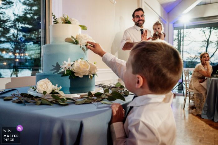 Fotografia documentaria dal luogo di nozze del Lago Pearl Wrentham, Massachusetts, di un bambino che raggiunge la torta nuziale