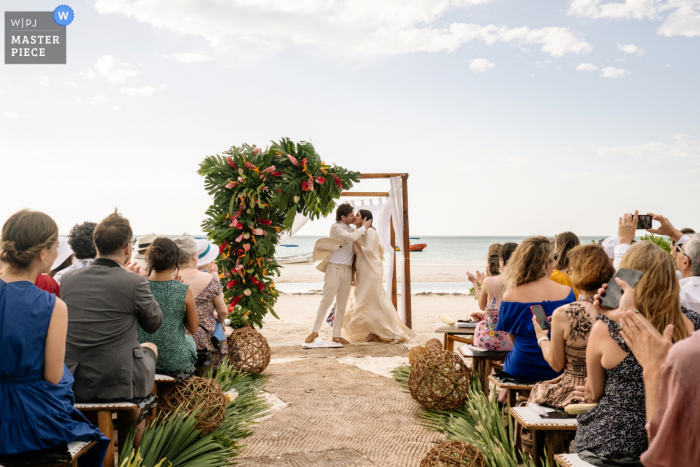 Documentary photography from a wedding venue in Holbox Island in Mexico showing the bride and groom kiss at end of beach ceremony