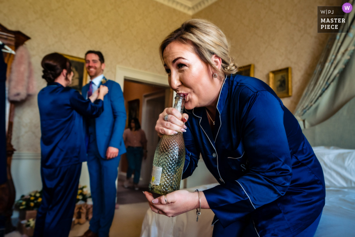 Dokumentarfotografie aus dem Hochzeitsort Somerley House in Hampshire von einer Brautjungfer, die Prosecco aus der Flasche trinkt