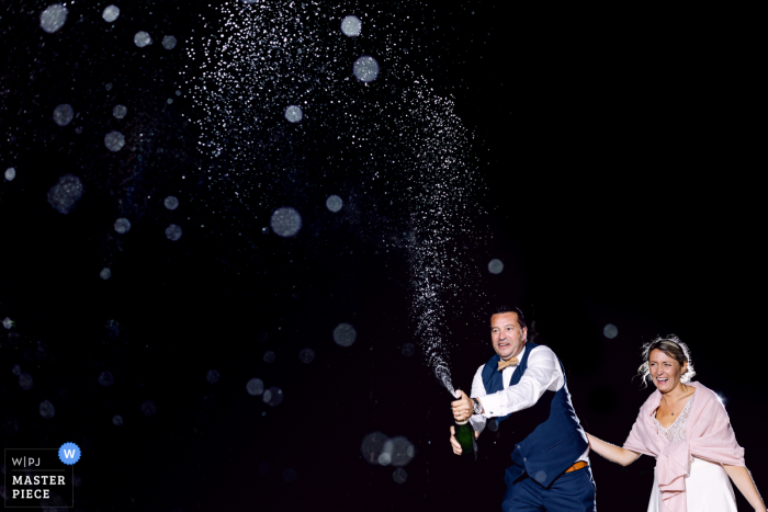 Best wedding photography from a Vendee venue, L'orangerie du Chateau showing The groom is popping champagne at night outdoors