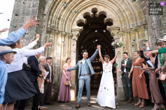 Dokumentarfotografie aus einer Hochzeitskirche in Seilhac, Nouvelle-Aquitaine, von Braut und Bräutigam, die draußen mit Familie und Gästen heiraten