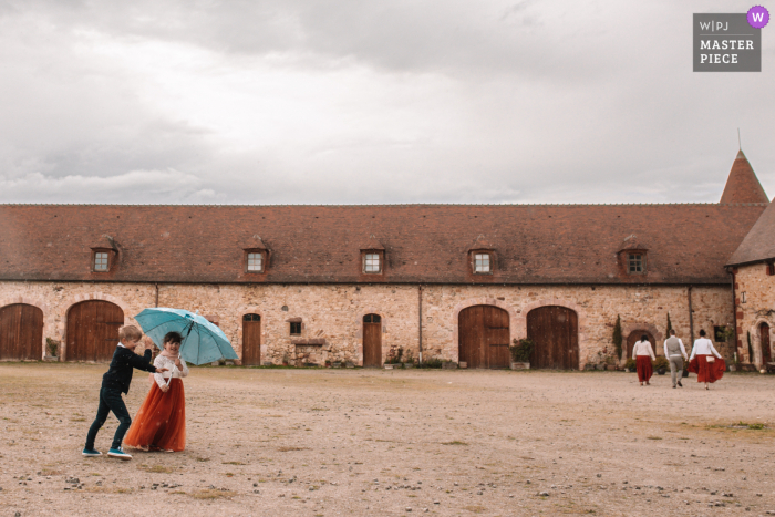 Beste Hochzeitsfotografie vom Veranstaltungsort Chateau de la Crete im französischen Departement Manche, Normandie von Kids mit Regenschirm, der hineingeht, weil es regnet