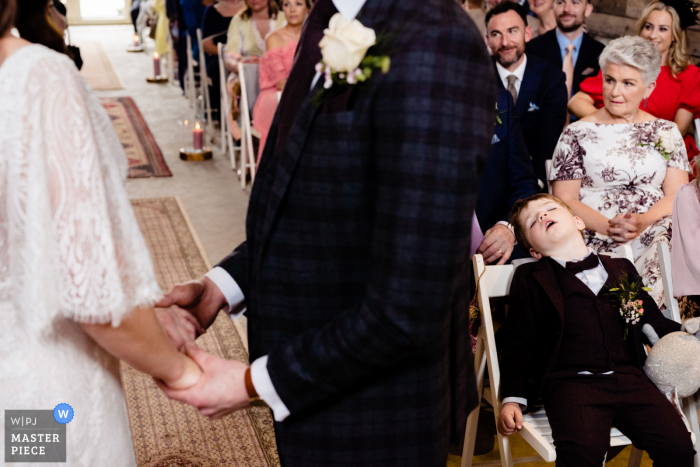 Der Dokumentar-Hochzeitsfotograf am Veranstaltungsort Cloughjordan House in Tipperary, Irland, hat diesen Pagenjungen beim Nickerchen während des Gelübdes festgehalten