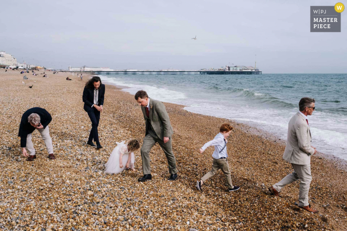 Trouwfoto in Londen vanaf het strand met gasten die rotsen op het water oppakken en overslaan