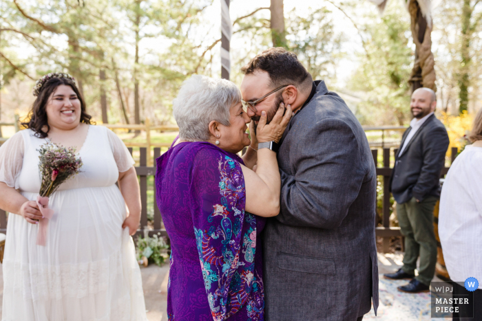 Documentaire huwelijksfotograaf in een ouderlijk huis in Manassas, Virginia legde de moeder van de bruidegom vast die hem feliciteerde na de ceremonie terwijl de bruid toekijkt