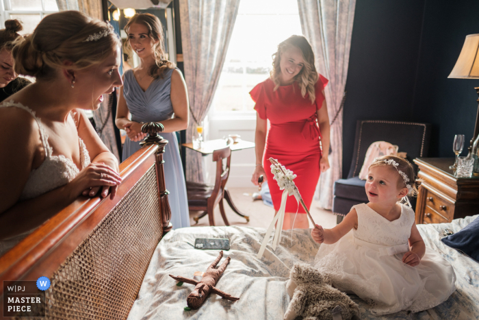 Imagen de la boda de Prestwold Hall de un evento de Leicestershire que muestra a la niña de las flores, mostrando a la novia su varita de flores, mientras su orgullosa madre mira al fondo