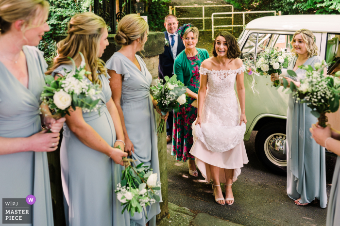 Imagen de la boda de West Sussex desde fuera de la iglesia de St Marys en Fittleworth que muestra a la novia saludando con entusiasmo a sus damas de honor en la puerta de la iglesia Imagen de la boda de West Sussex desde fuera de la iglesia de St Marys en Fittleworth que muestra a la novia saludando con entusiasmo a sus damas de honor en la puerta de la iglesia