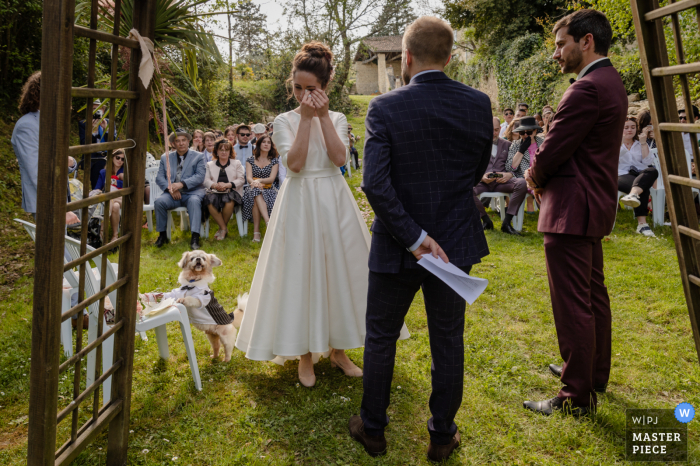 Beste huwelijksfotografie van een locatie in de Gers, Chartreuse de Dane, waarop de bruid huilt, terwijl de hond en de gasten worden bewogen tijdens de tuinceremonie in de buitenlucht