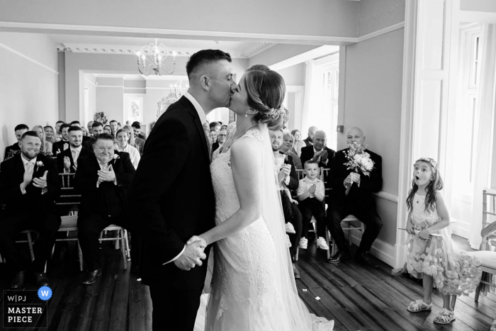 La mejor fotografía del lugar de la boda de Ashton Lodge Country House en Warwickshire, Reino Unido, capturando la expresión de sorpresa de las hijas de los novios durante el primer beso