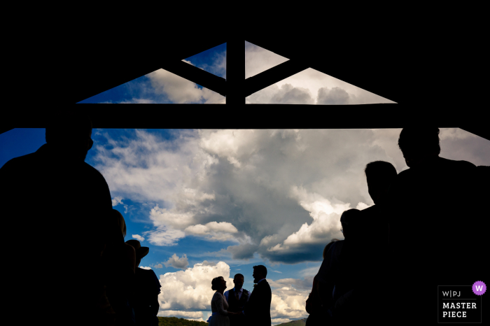 Dokumentarfotografie aus der Hochzeitslocation The Barn at Boyden Farm in Vermont, die zeigt, wie das Brautpaar mit blauem Himmel und geschwollenen Wolken im Rücken geheiratet hat