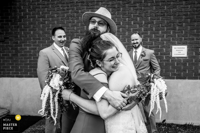 Immagine del matrimonio dell'Ontario in bianco e nero da una sala per banchetti creata mentre la sposa viene inondata di abbracci dal fratello e dalla matrona d'onore subito dopo la cerimonia