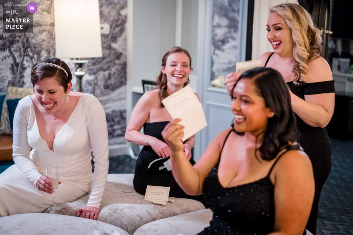 Old Town Alexandria based wedding and event photography at The Alexandrian Hotel of The bride and her bridesmaids laughing while reading letters in the getting ready room