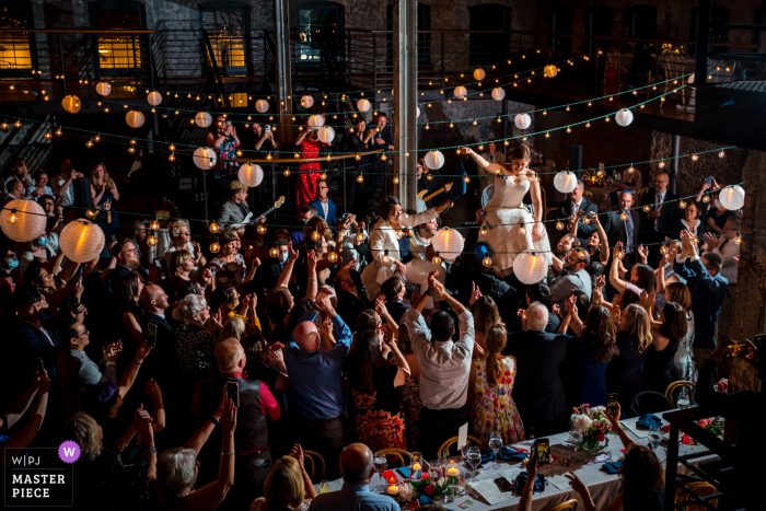 Die Fotografie des Hochzeitsortes Winslow Baltimore in Maryland zeigt zwei Bräute, die während des Hora-Tanzes in die Luft gehoben wurden