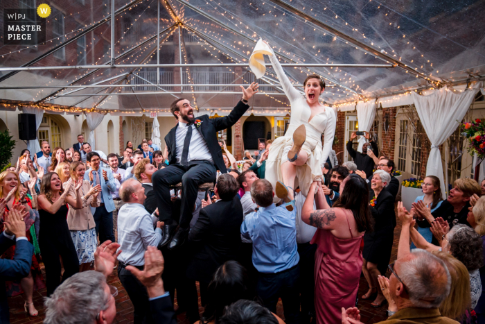 Casamento baseado em Alexandria e fotografia de eventos no The Alexandrian Hotel mostrando a noiva e o noivo sendo levantados no ar durante a hora enquanto a noiva rouba o guardanapo Casamento baseado em Alexandria e fotografia de eventos no The Alexandrian Hotel mostrando a noiva e o noivo sendo levantados no ar durante a hora enquanto a noiva rouba o guardanapo