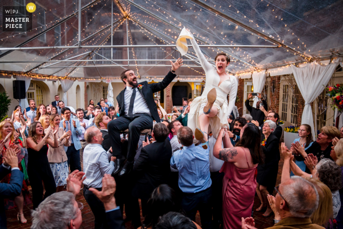 Fotografia di matrimoni ed eventi con sede ad Alessandria presso l'Hotel Alexandrian che mostra gli sposi sollevati in aria durante l'ora mentre la sposa ruba il tovagliolo