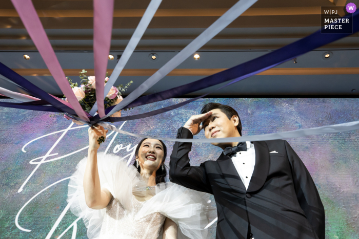 Thailand documentary-style wedding image from Conrad Bangkok Hotel of the couple as the bride holds up the bouquet and ribbons for the game