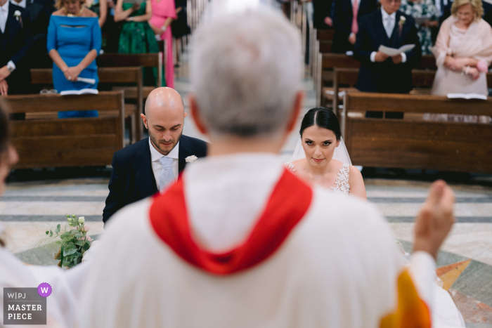 Photographie de mariage de style éditorial des Pouilles prise de derrière le prêtre pendant la cérémonie