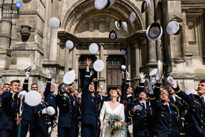 A wedding photographer in Eure, France created this image of The groom's military comrades toss their caps into the air at the church