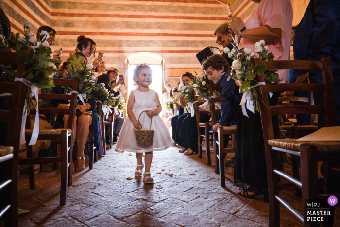 Beste documentaire trouwfoto van Chiesa di Colle Ciupi in Siena, Italië, waarop het kleine bloemenmeisje te zien is dat door het gangpad bij de kerk loopt