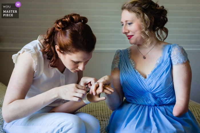 Fotografie im Dokumentarstil von einer Haute-Marne-Hochzeit in Langres, Frankreich, die die Braut festhält, die ihrer Schwester das Blumenarmband um den Arm bindet