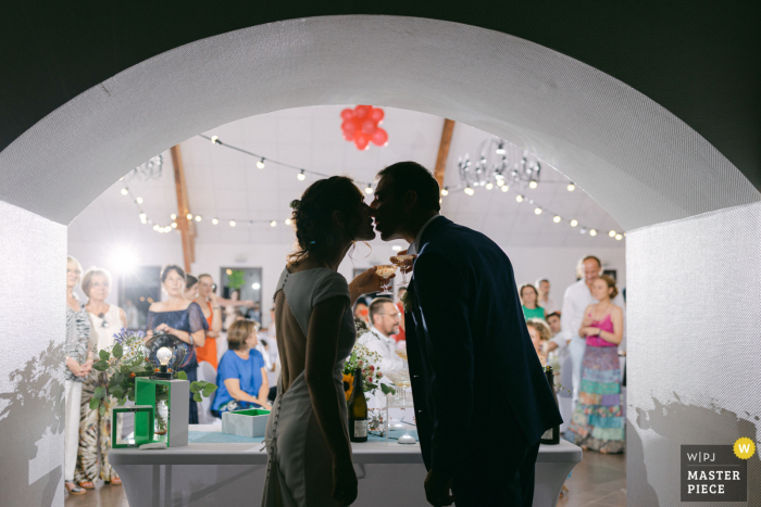 The bride and groom shared a romantic kiss in silhouette as champagne flowed from a fountain at their wedding reception France winning image from the best documentary style wedding photography contest in the world showing a Champagne fountain during dinner in a silhouette shot