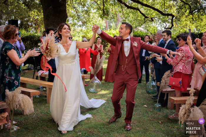 The newlyweds celebrated their union with a joyful ceremony, captured by a France candid wedding photographer, as they walked across the grass under the trees to their cheering guests A France wedding photographer captured the End of the ceremony as the newlyweds cross the guard of honour