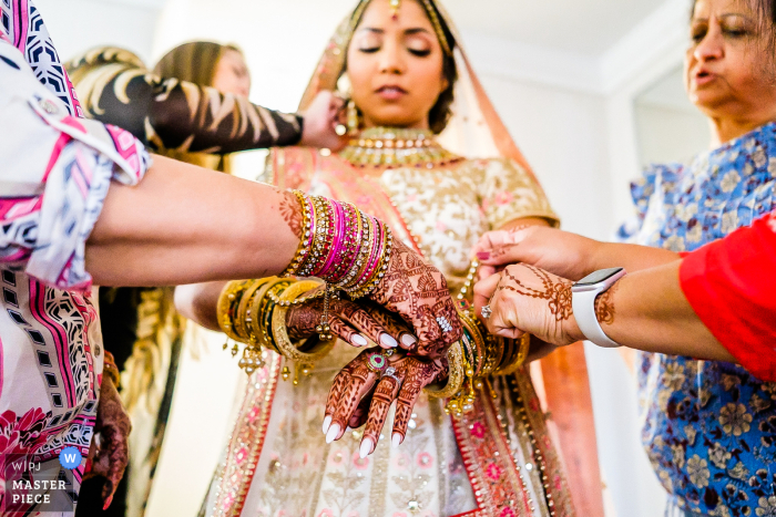 La sincera fotografía documental de bodas de Michigan en The Meridian Banquet and Events Hall en Farmington Hills capturó a esta novia india que recibía ayuda con sus brazaletes