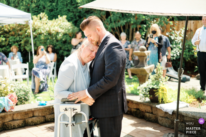 Photo by: <a href="https://wpja.com/contests/2022-v02/best-wedding-photographers/2667085">Benjamin Wagner - Mercer Island Washington</a> Washington documentary-style wedding image from a Lake Tapps private home showing The mother of the groom, who's battling brain cancer, insists on making the traditional mother and son dance happen