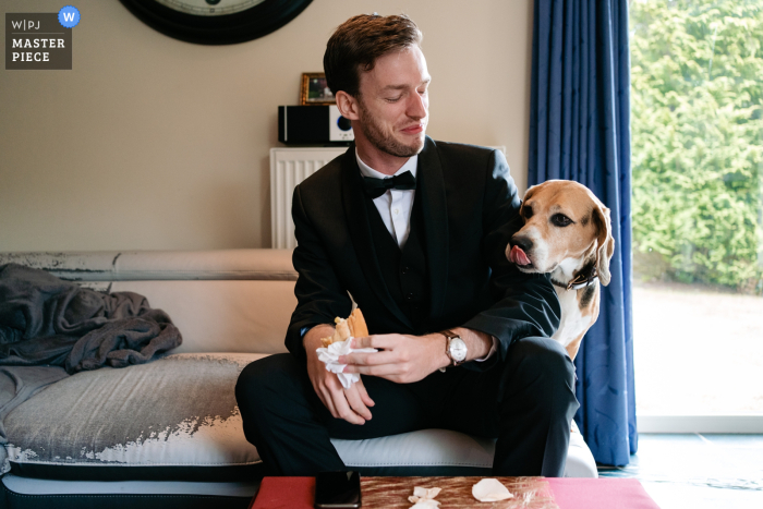 Belgium documentary wedding photography contest winning image showing Someone of the groom's wedding party is eating lunch and the groom's dog is interested too