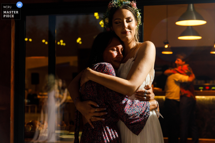 World-class documentary wedding image from Gradina cu Licurici in Romania showing Bride and her aunt hugging at the end of the reception venue party 