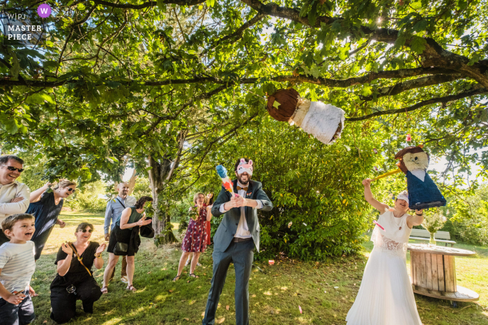 Photographie de mariage + fugue dans le Morbihan en Bretagne, France sur le lieu de réception en plein air avec les mariés cassant des piñatas sous les arbres