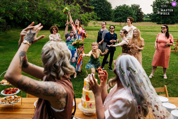 Imagen ganadora de Yorkshire del mejor concurso de fotografía de bodas estilo reportaje del mundo en Crayke Manor que muestra a la pareja lanzando sus ramos de flores a sus invitados en el césped detrás de ellos