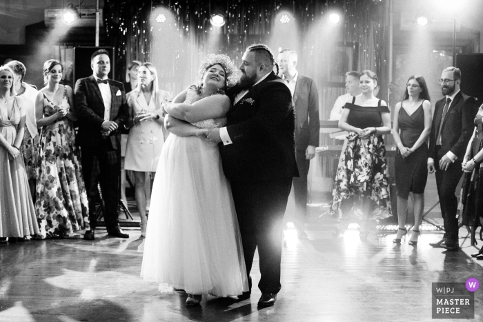 Imagem vencedora do concurso de fotografia de casamento documental da Polônia no Folwark Tworzyjanki capturando a primeira dança em BW sob as luzes do palco do DJ