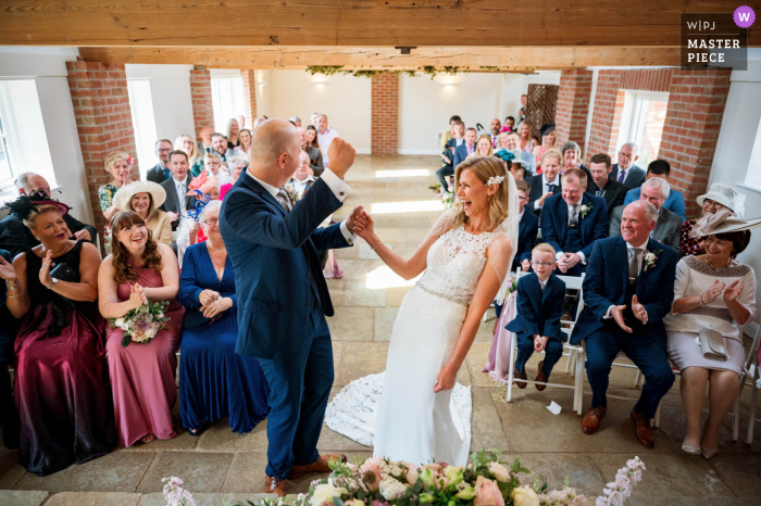 Ein Hochzeitsfotograf der Hanbury Wedding Barn erstellte dieses Bild einer glücklichen britischen Braut und eines Bräutigams während der Trauung im Innenbereich