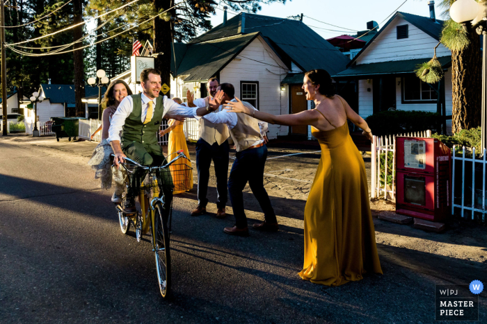 On the way to their wedding reception at South of North Brewing Co in South Lake Tahoe, CA, the bride and groom ride a tandem bike and high-five their wedding party as they celebrate their love and union