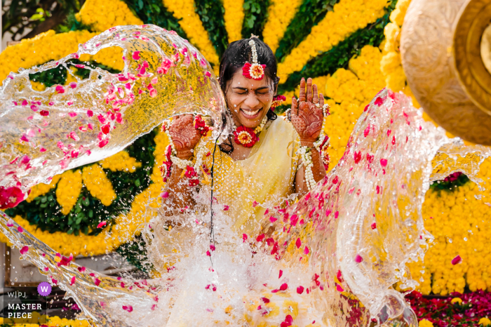 Amici e parenti vengono catturati mentre lanciano acqua Haldi sulla sposa durante una cerimonia Haldi in una fotografia di matrimonio Una cerimonia Haldi in Karnataka, in India, cattura amici e parenti che lanciano acqua Haldi sulla sposa