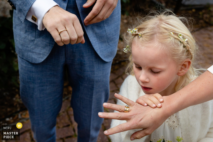 The wedding photojournalism image captures an intimate moment as the bride and groom's hands are visible, and the young daughter looks curiously at the bride's ring In the Netherlands city of Overveen, a Netherlands photographer captured a wedding reportage image with just the bride and groom's hands visible, while the young daughter looks closely at the ring