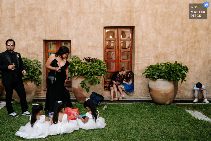 Captured during a unique outdoor wedding, the documentary image shows guests socializing while the children play on the grass during the cocktail hour At the beautiful Quinta Real in Oaxaca City, Mexico, a wedding picture from outside on the grass next to the building door during the cocktail hour